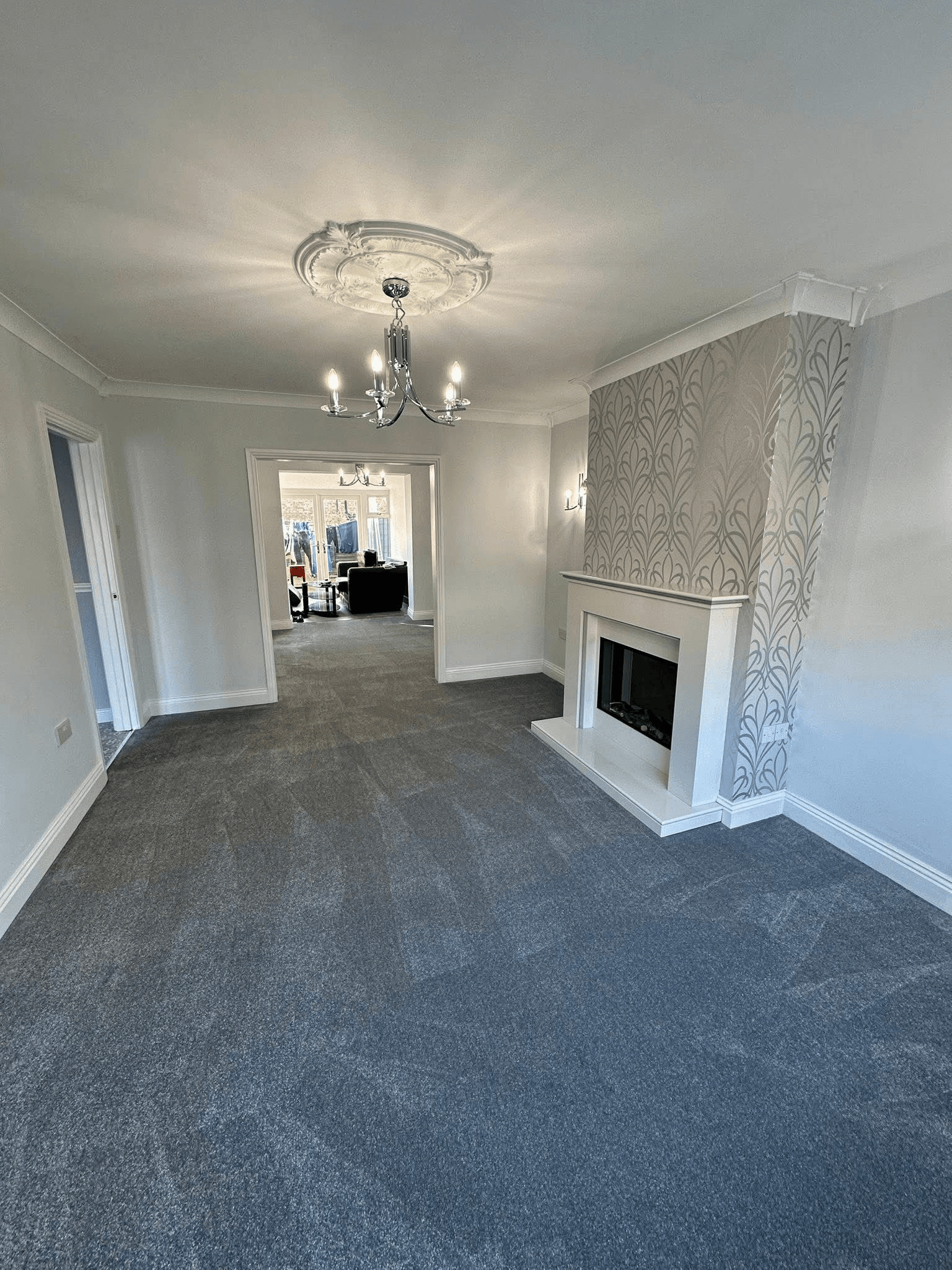 Charcoal carpet fitted in spacious living room with chandelier and decorative fireplace