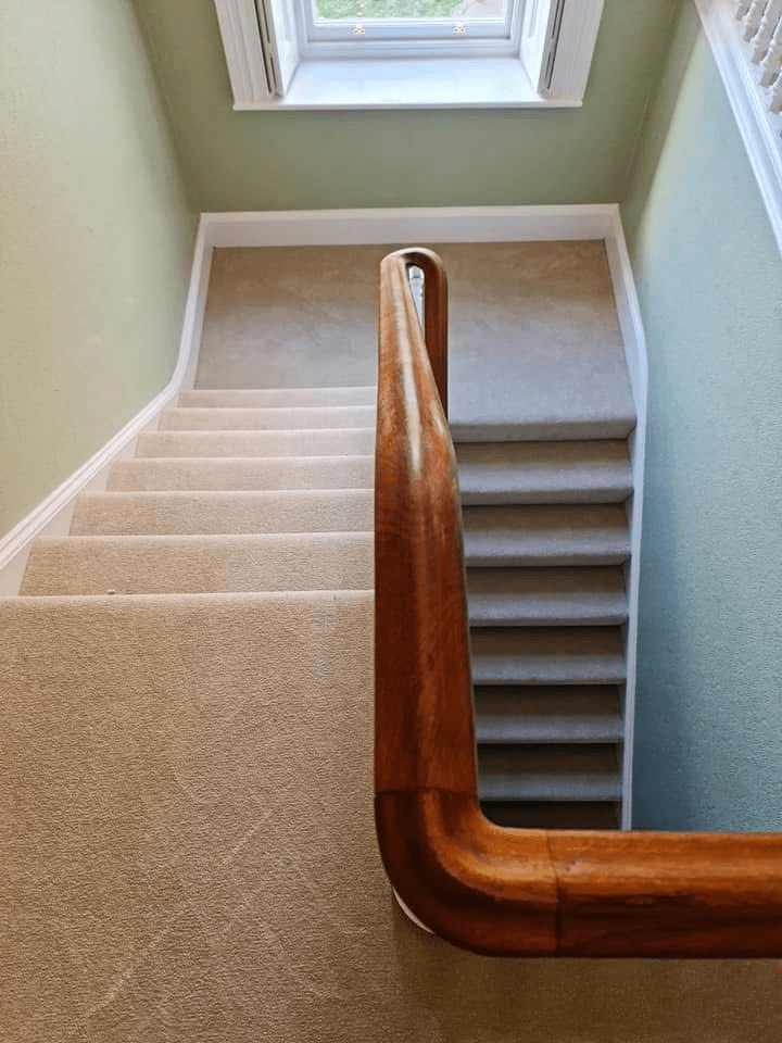 Beige carpet fitted on staircase with polished wooden banister and natural light from skylight