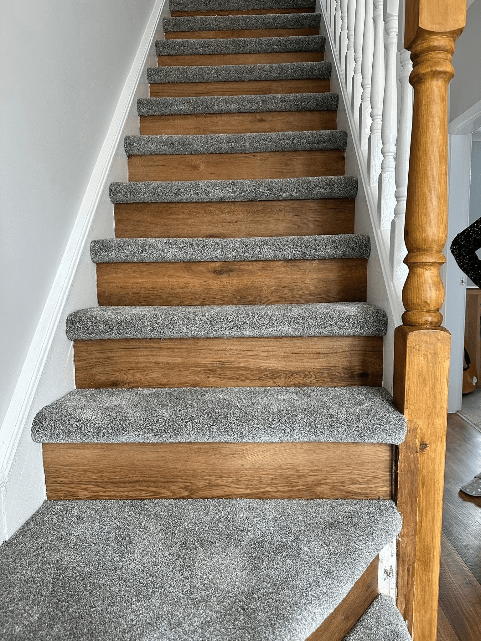 Grey carpet fitted on stair treads with exposed oak risers and banister