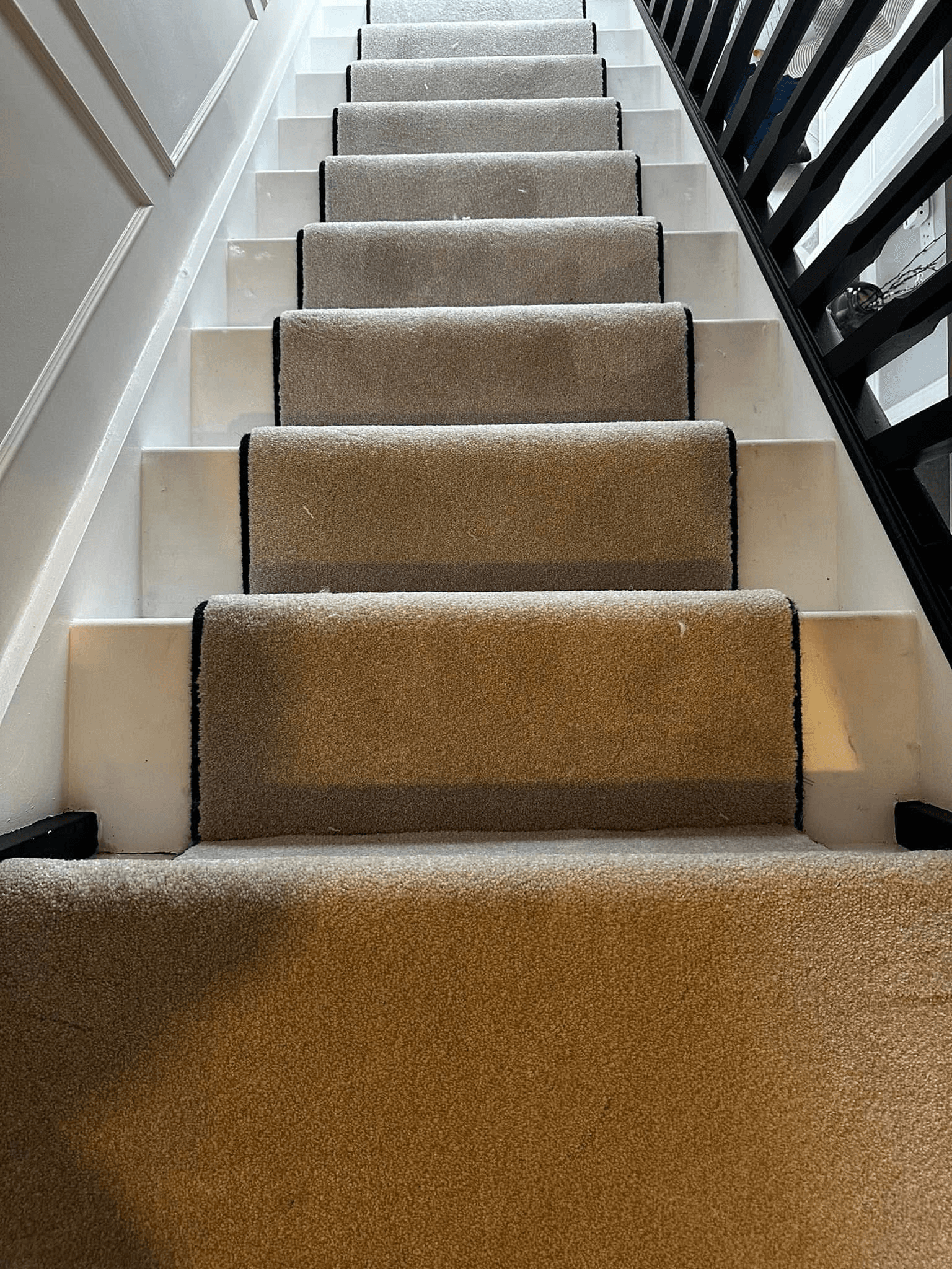 Tan stair runner with black bound edging fitted on white-painted staircase
